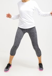 Camiseta deportiva Nike de manga larga blanca combinada con leggins negros con un diseño ondulado y zapatillas negras con suelas rosas.