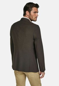 Donkerbruine blazer van gestructureerde stof, met een enkele split aan de achterkant en knoopmanchetten, gecombineerd met lichtbeige broeken.