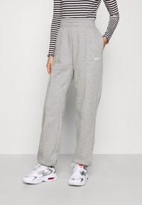Persona que lleva pantalones de chándal grises de talle alto de Nike, una camiseta de manga larga a rayas en blanco y negro, y zapatillas blancas de Nike con detalles en rojo y azul.