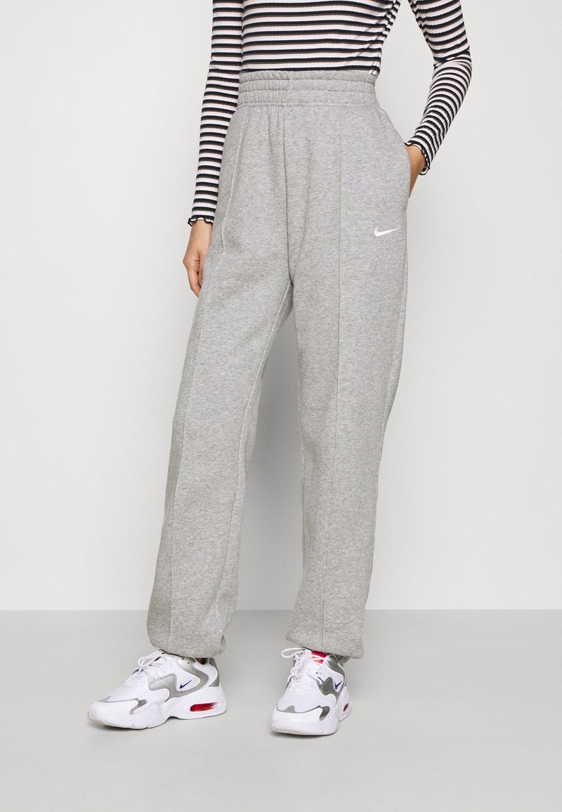 Persona que lleva pantalones de chándal grises de talle alto de Nike, una camiseta de manga larga a rayas en blanco y negro, y zapatillas blancas de Nike con detalles en rojo y azul.