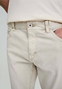 Helle beige Jeans aus Denim mit Knopfverschluss und seitlichen Taschen. Verfügt über subtile Nähte und eine glatte Textur. Lockerer Schnitt dargestellt.