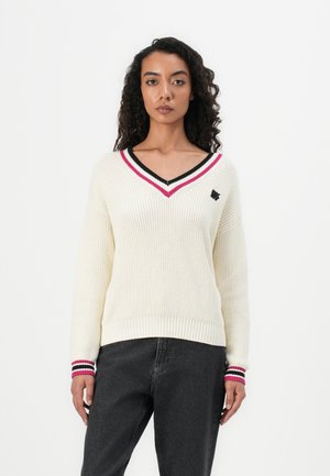 Kremfarget strikket genser med dyp V-hals, med svart og rosa striper ved kragen og mansjettene, samt en liten svart logo på brystet.