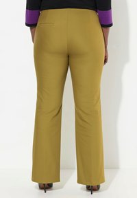 Senapsgula utsvängda byxor med en slät yta, med en bakficka. Bärs tillsammans med svarta högklackade skor, mot en neutral bakgrund.