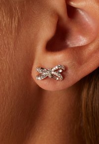 Silberne bogenförmige Ohrringe mit filigranen Details, besetzt mit kleinen glitzernden Steinen, die an einem Ohr positioniert sind.
