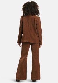 Brown corduroy suit with a fitted blazer and flared pants. The fabric has a textured finish and a smooth, polished appearance.