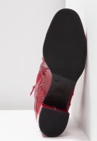 Chaussure en cuir rouge avec semelle noire lisse et talon bloc, taille 4 1/2, positionnée verticalement sur fond blanc.