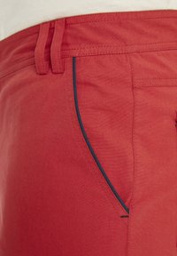 Rote Hose mit glatter Textur, ausgestattet mit einer seitlichen Tasche, die in Marineblau eingefasst ist. Entworfen mit Gürtelschlaufen und geraden Beinen.