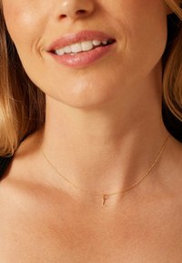 Collier en or avec une chaîne fine et un petit pendentif en forme de 'L', vue en gros plan de la zone du cou, mettant en valeur le design délicat et la finition métallique.