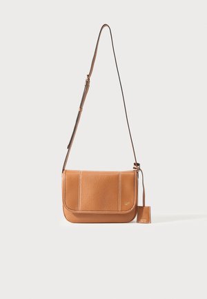 Hnedá kožená kabelka cez rameno s nastaviteľným remienkom, zapínaním na klopu a malou pripojenou zveskou na jednoduchom svetlom pozadí.