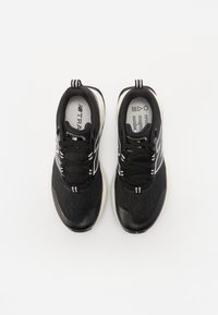 Chaussures de sport noires avec une tige en tissu texturé, des accents blancs et une semelle rembourrée. Comprend des lacets et un logo sur la languette.