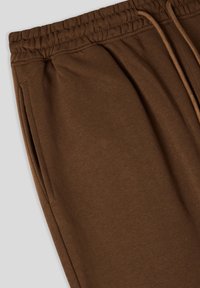 Brązowe dresy wykonane z miękkiej bawełny, z elastycznym pasem, sznurkiem do regulacji i bocznymi kieszeniami. Gładka tekstura i luźny krój.