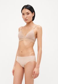 Reggiseno beige chiaro e mutandine coordinate realizzate in tessuto morbido. Il reggiseno ha una forma triangolare, spalline regolabili e un semplice bordo scallopato sulle mutandine.