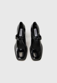 Chaussures Mary Jane en cuir verni noir avec un bout carré, une seule sangle ajustable et une semelle plate. Présente des détails de couture audacieux.