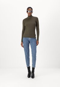 Olive ribbed turtleneck sweater paired with light blue jeans and black ankle boots. Model wearing reflective sunglasses.