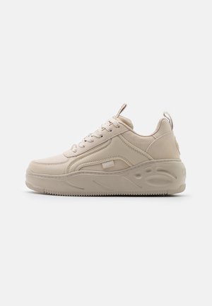 Beige sneaker med kraftig sål, snørebånd foran, løfteflapper på tungen og hælen samt tekstureret design på den tykke sål.