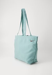 Bolsa de lona en azul claro, con el logotipo de Nike en color marrón. Dos largas correas planas para el hombro. Forma rectangular simple.