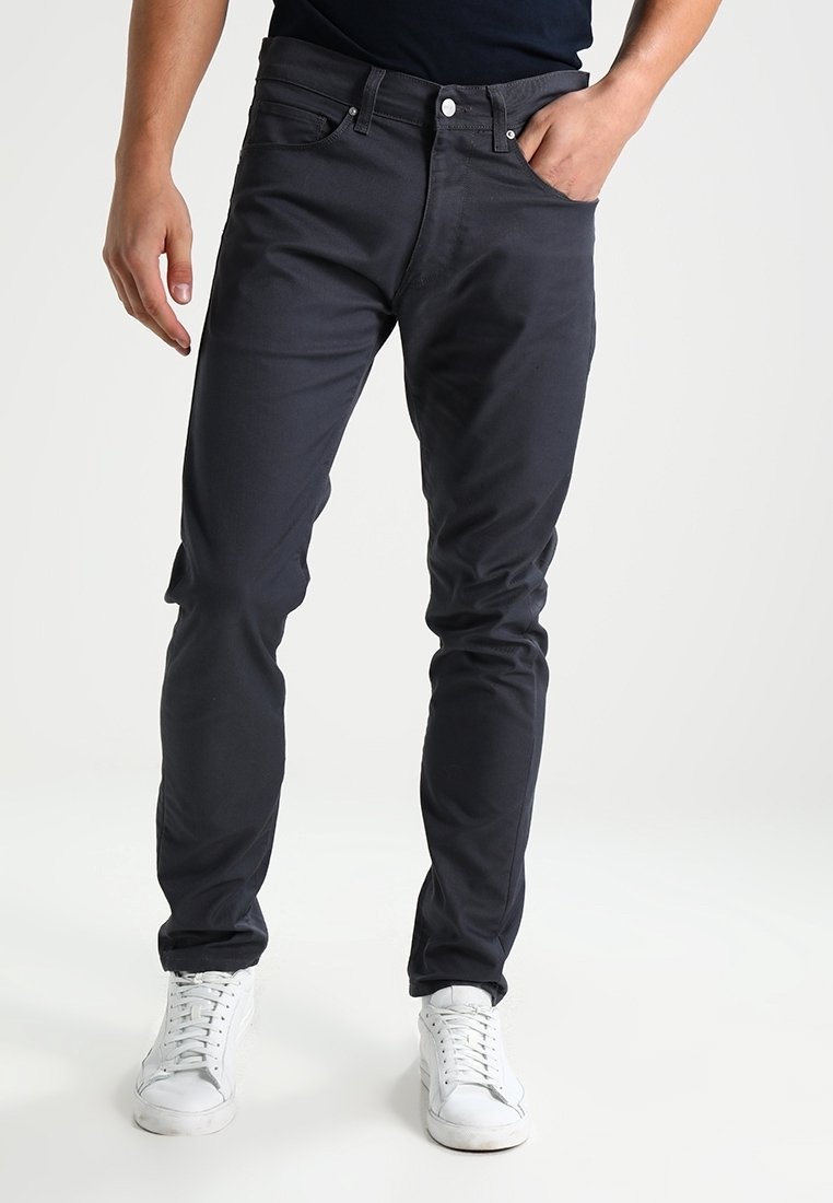 Mørkegrå jeans lavet af bomuld, med slim fit, fem-lomme design og en knaplukning. Kombineret med hvide sneakers.