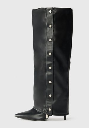 Botas de salto alto em pele preta com um design ajustado, bico fino e detalhes em botão de pressão prateado ao longo do lado.