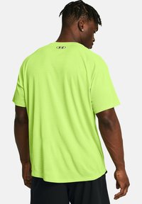 Neon-grünes T-Shirt mit kurzen Ärmeln und runder Ausschnitt, mit einem Logo auf dem Rücken, aus einem glatten, texturierten Stoff.