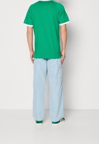 Grön t-shirt med vit krage, i kombination med ljusblå, vida cargobyxor; svarta och vita randiga sneakers fulländar outfiten.