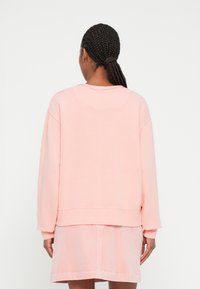 Sweatshirt oversized em rosa claro com decote redondo e punhos canelados. O tecido parece suave, com uma textura lisa.