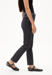 Zwarte denim jeans met een slim fit, vijf zakken en zichtbare stiksels. Draagt een paar zwarte ballerina's met metalen accenten en een band.