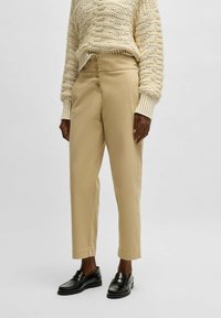 Beige, skräddarsydda byxor med en slät yta, med hög midja och treknapprad framtill. Matchas med svarta loafers.