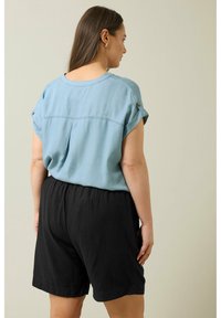 Blusa azul claro de manga corta con puños enrollados, presenta un pliegue en la parte trasera. Combinada con pantalones cortos negros de corte holgado, hechos de una tela texturizada.