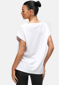 Camiseta blanca de manga corta con un corte relajado, escote redondo y mangas enrolladas. Textura de tejido suave, con un dobladillo ligeramente curvado.