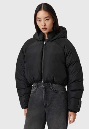 Fekete, rövidített puffermellény kapucnival, elől cipzárral záródik, bordázott passzékkal rendelkezik, sima, fényes textúrájú. Sötét farmerrel párosítva.