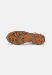 White sneaker sole with a textured brown rubber outsole featuring circular and linear tread patterns. Logo embossed on the side.