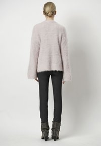 Langsleeve, fluffy cardigan in zacht pastelroze, met een iets cropped zoom. Gecombineerd met strakke zwarte leggings en grijze enkellaarzen.