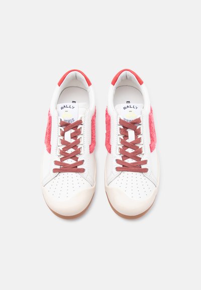 Λευκά δερμάτινα χαμηλά sneakers με ροζ χνουδωτές πλευρικές επενδύσεις, καφέ κορδόνια, διάτρητες μύτες και κόκκινες λεπτομέρειες στη φτέρνα, απόψη από πάνω.