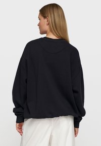 Schwarzer übergroßer Pullover mit rundem Ausschnitt, überschnittenen Schultern und geripptem Saum. Glattes Material mit minimalen Nähdetails.