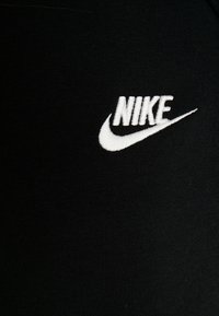 Svart tyg med en vit broderad Nike-logotyp som visar en swoosh och text i fet, tydlig stil, med en mjuk textur.