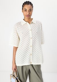 Kortermet skjorte i off-white strukturert stoff med geometrisk mønster, med knappefront og kontrasterende krage. Matchende med løse bukser.