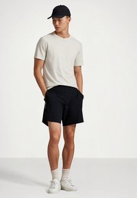 Helehall hall T-särk, mustad lühikesed püksid, valged tennised ja must nokamüts. Taperdatud lühikesel püksil on küljetaskud ja detailseks aktsendiks on logo.