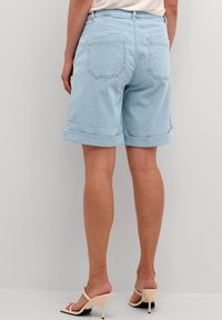 Pantaloni shorts in denim a righe azzurro chiaro con risvolti, dotati di due tasche posteriori e un taglio dritto. Texture morbida e design casual.