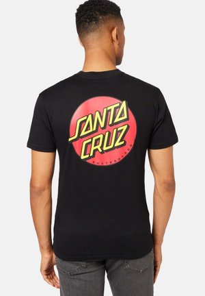 Camiseta negra de manga corta, con un gran logo de círculo rojo y el texto amarillo "SANTA CRUZ SKATEBOARDS" en la parte posterior.