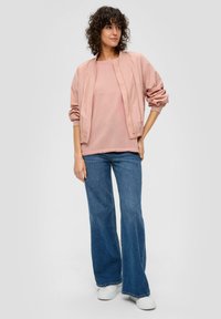 Giacca bomber rosa chiaro su una maglietta rosa, abbinata a jeans svasati blu e sneakers bianche. Tessuti morbidi con un taglio rilassato.
