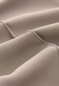 Gros plan d’un tissu côtelé beige avec une couture visible et des plis doux montrant la texture et les détails des coutures.