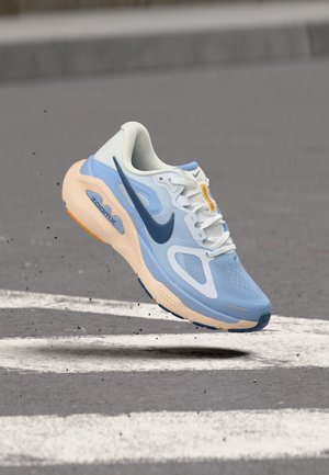 Világoskék és bézs Nike futócipő tengerészkék jelzéssel, légtérben egy zebrán egy aszfaltúton.