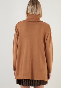 Brauner Strickpullover mit Stehkragen und oversiziger Passform. Der Stoff wirkt weich und texturiert, hat lange Ärmel und einen geraden Saum.