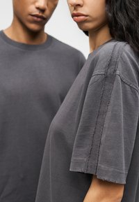 Γκρι μπλουζάκια με άνετη εφαρμογή, με ακατέργαστες άκρες και ορατές ραφές κατά μήκος των μανικιών. Απαλό βαμβακερό ύφασμα.