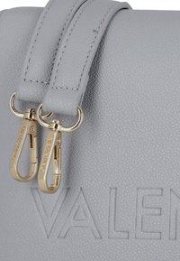 Borsa a mano in pelle grigia con superficie testurizzata, dotata di due zip dorate e logo "VALENTINO" impresso.