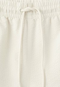 Gros plan sur un short blanc avec une ceinture élastique, un tissu texturé et un cordon noué au centre devant.