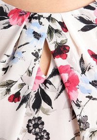 Floral print fabric featuring pink, blue, and black flowers on a light background. Keyhole design at the neckline with soft texture.