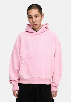 Oversized pink hoodie made of soft fabric, featuring a front pocket, a drawstring hood, and ribbed cuffs with a relaxed fit.