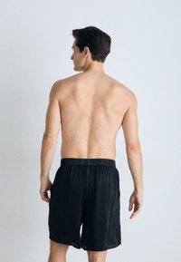Black cotton shorts with an elastic waistband, seen from the back. The material appears lightweight with a soft texture.