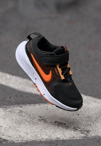 Schwarzer und orangefarbener Sportschuh mit Mesh-Obermaterial, gepolsterter Sohle und Riemenschluss. Verfügt über ein Logo und kontrastierende Akzente.